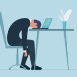 疲労困憊で机に伏せる男性